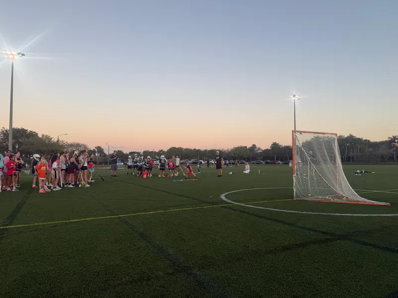 The lacrosse field, goal and lights at sunset with a practice underway in the distance