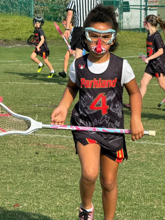 A Redhawks girl in goggles and a Parkland jersey runs with her stick