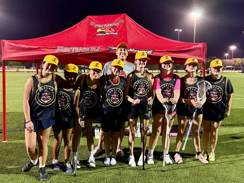 A Redhawks girls team in black pinnies and yellow caps lines up under the red Redhawks tent at night
